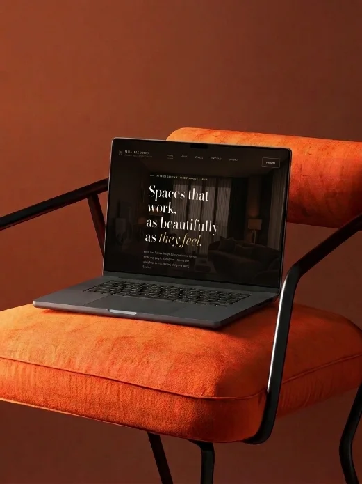 Laptop on a burnt-orange chair showing the Maya Luxe Homes website homepage